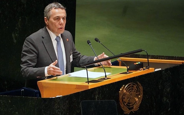 Il Consigliere federale Cassis siede al leggio e parla. Il logo dell'ONU è visibile in primo piano.
