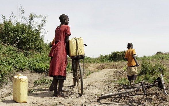 Two children of African origin carry yellow cans on bicycles.