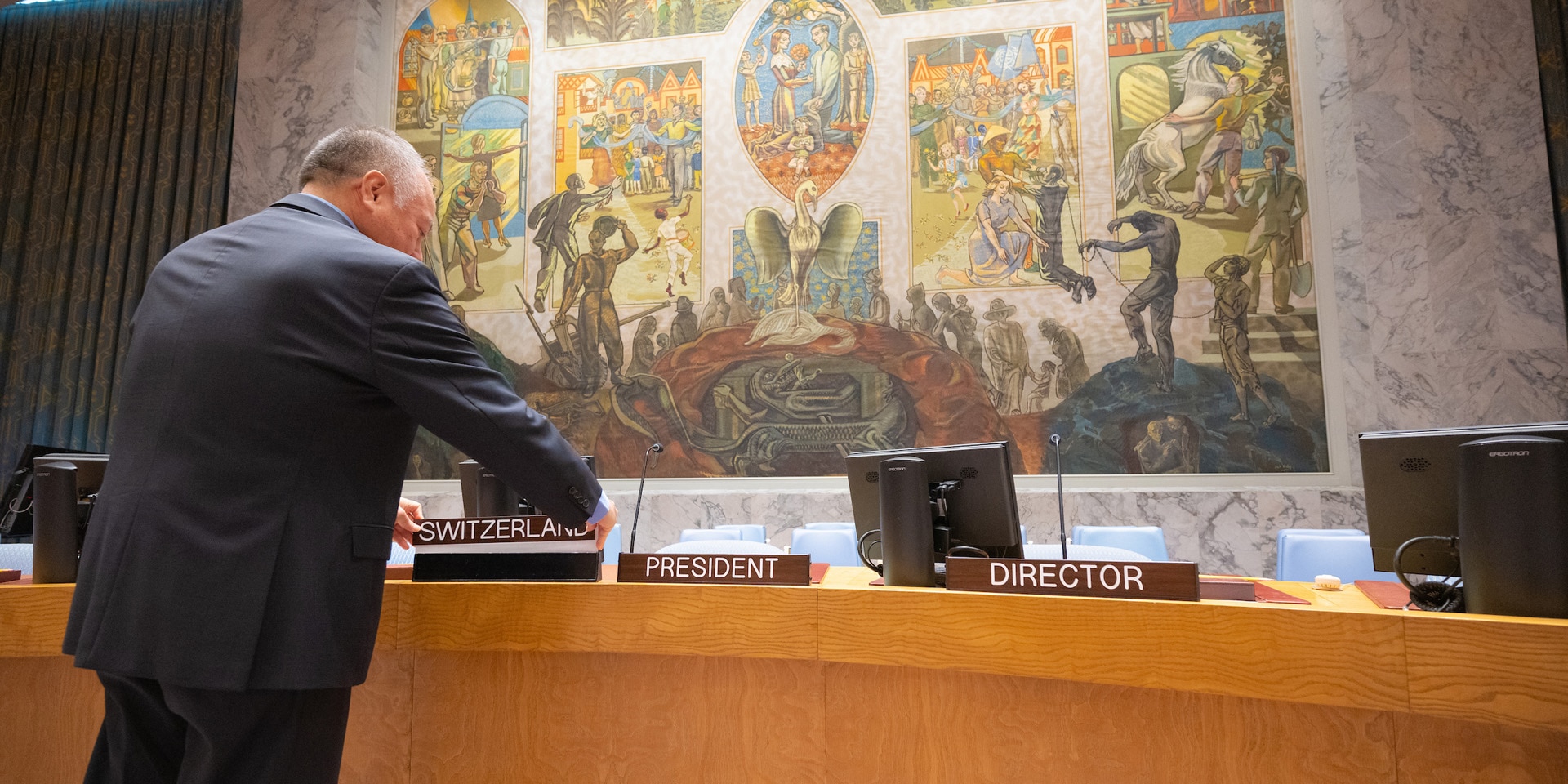 A UN official placing a sign reading 'Switzerland' in the president's place at the horseshoe-shaped table of the UN Security Council.