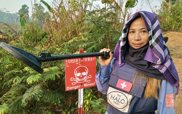 Una sminatrice di «Halo Trust» con la croce svizzera, accanto a un campo minato.