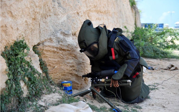 A man wearing protective equipment is defusing an explosive device.