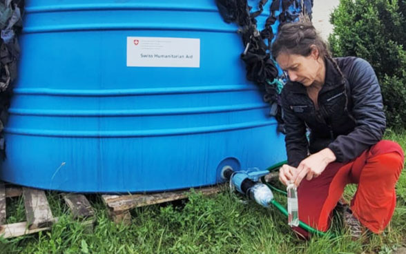 Eine Frau kniet neben einem blauen Wassertank und lässt Wasser in eine Flasche fliessen.