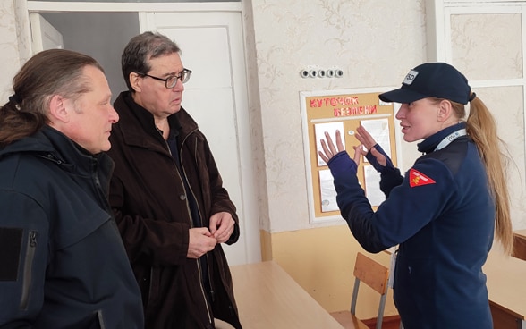  A woman in FSD uniform explains something to two men, listening attentively.