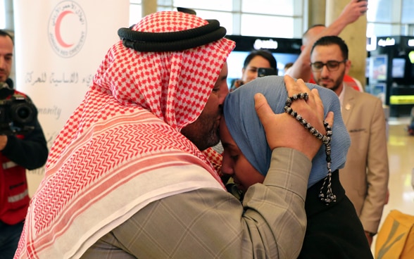 Un homme avec un keffieh sur la tête embrasse sa fille sur le front.