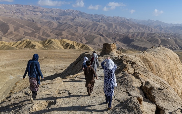 In einer kargen bergigen Landschaft in Afghanistan gehen vier Mädchen und ein Junge einem Bergkamm entlang.