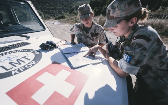 Two women of the Swiss Armed Forces look at a map on the bonnet of a jeep.
