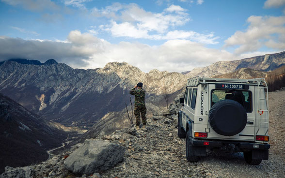 Ein Angehöriger der Schweizer Armee steht neben einem Einsatzfahrzeug und beobachtet ein Tal in Bosnien und Herzegowina.