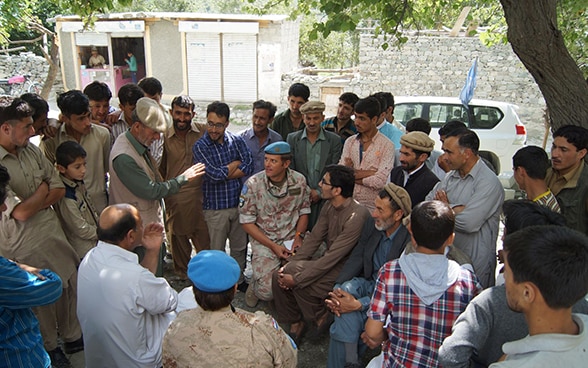 Un osservatore militare svizzero siede in mezzo a una folla di persone in un villaggio della regione del Kashmir e ascolta ciò che hanno da dire.