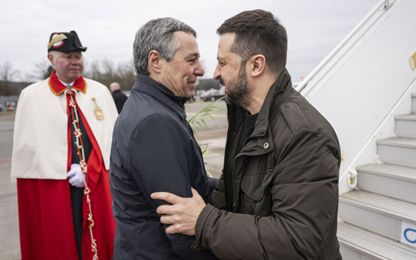 Le conseiller fédéral Cassis salue chaleureusement le président Selenskyj. Un huissier se trouve à l’arrière-plan.