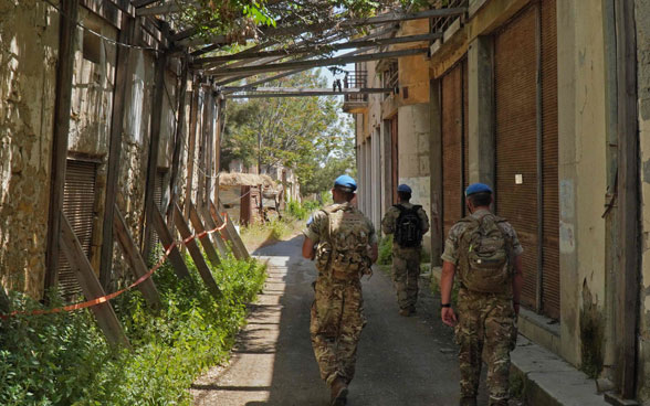 Members of the UN peacekeeping force UNFICYP walk through an alley between dilapidated buildings in the buffer zone.