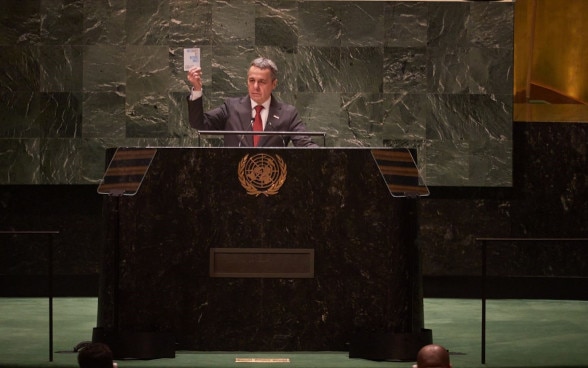Ignazio Cassis à la tribune de l'Assemblée générale des Nations Unies à New York. Il tient dans une main un exemplaire de la Charte de l'ONU.