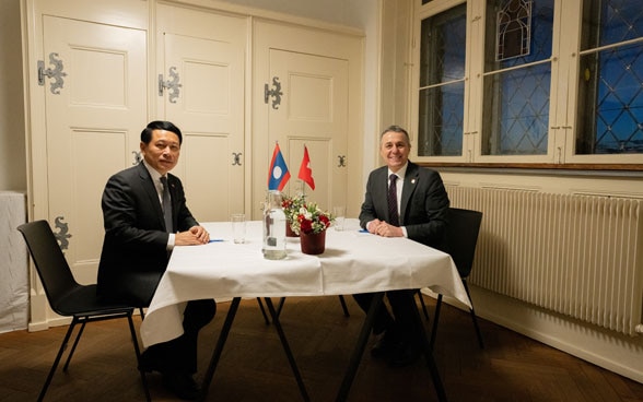 Ignazio Cassis und Saleumxay Kommasith sitzen an einem Tisch, auf dem die Flaggen ihrer Länder platziert sind.