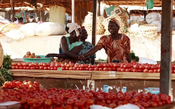 Deux femmes derrière un stand de marché rempli de tomates mûres en Ouganda.