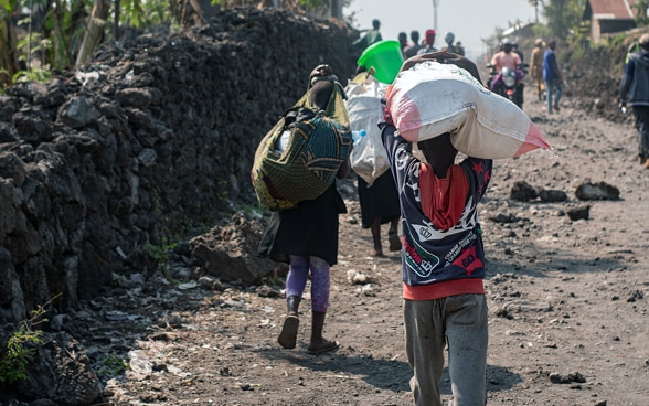 Kongolesische Kinder gehen eine Strasse entlang und tragen ihr Hab und Gut auf dem Kopf.