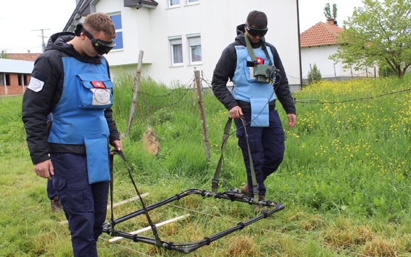 Minenräumer in Schutzanzügen suchen den Boden mit Detektoren nach Streumunitionsrückständen ab.