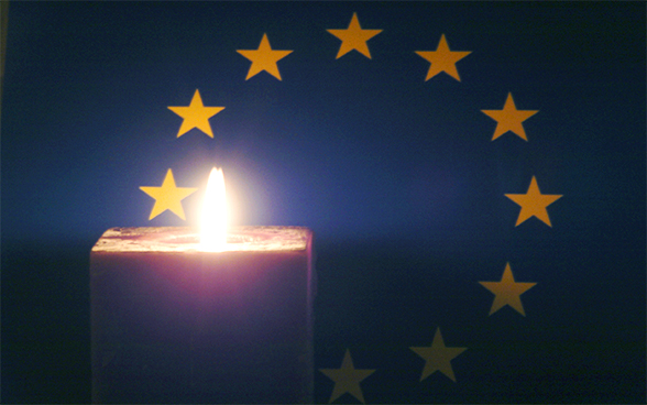 Foto einer Kerzenflamme vor der Europaflagge als Symbol für die Förderung der Menschenrechte