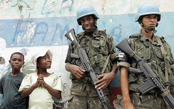 Due membri dell'ONU, con le armi a tracolla, vicino ad alcuni bambini sorridenti in occasione di una manifestazione organizzata dalla popolazione locale ad Haiti