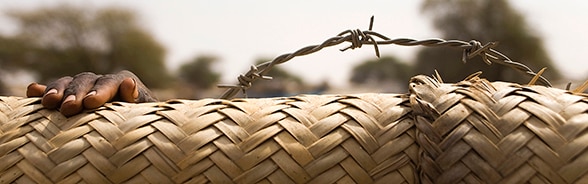 Hand of a child appearing behind the barbed wire fence of a camp for internally displaced persons (IDPs) in North Darfur