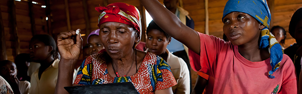 Two women from the African Great Lakes region – one looking at a document, the other with arm outstretched. 