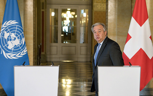 Le secrétaire général des Nations Unies António Guterres derrière deux pupitres entre les drapeaux suisses et onusiens