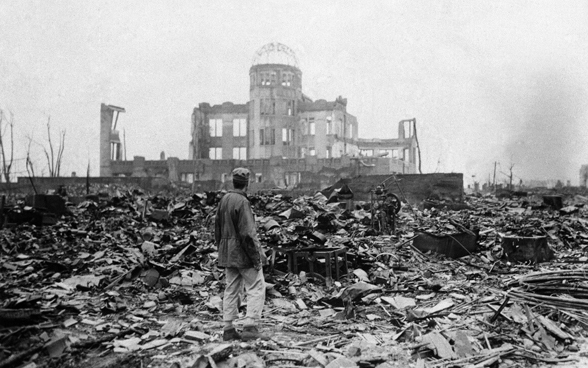 Ein Mann steht in Mitten von Trümmern und Ruinen, die der Kernwaffenabwurf auf Hiroshima angerichtet hat.