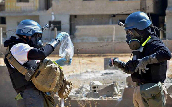 Zwei Experten in Schutzausrüstung wie Atemmasken, Helme, Schutzwesten und Handschuhe sammeln Proben ein, um sie auf Rückstände chemischer Waffen zu analysieren.