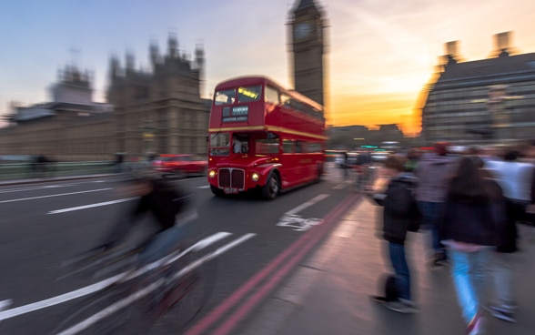 Un autobus rosso a due piani, tipico di Londra, passa davanti al Big Ben sul ponte di Westminster fino al tramonto