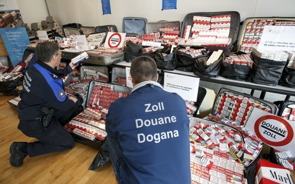 Una guardia di frontiera e un funzionario doganale presentano 3500 stecche di sigarette dopo un sequestro doganale all'aeroporto di Ginevra.