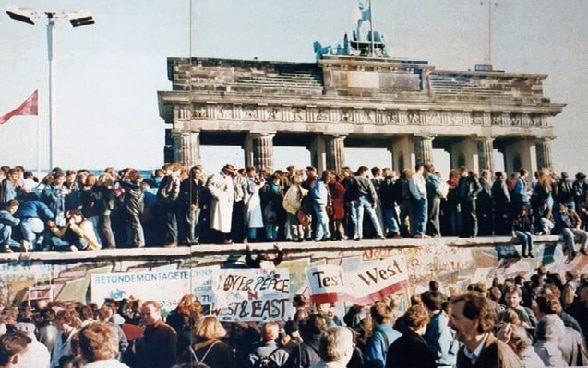 Menschen aus West- und Ostberlin stehen zu Hunderten auf Mauer nahe dem Brandenburger Tor.