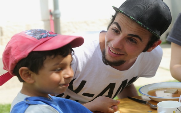 Assis côte-à-côte, un jeune homme et un petit garçon s'apprêtent à prendre leur repas au foyer d'enfants «PeCA». 