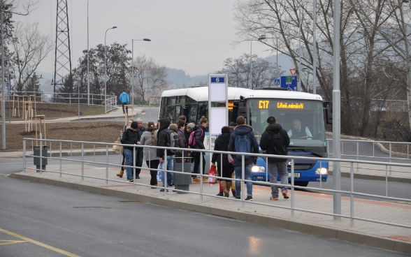 Eine kleine Menschenmenge besteigt einen lokalen Bus am neuen Busbahnhof - frisch gepflanzte Bäume und unbegrünte Wiesen zeugen vom Revitalisierungsengagement. 