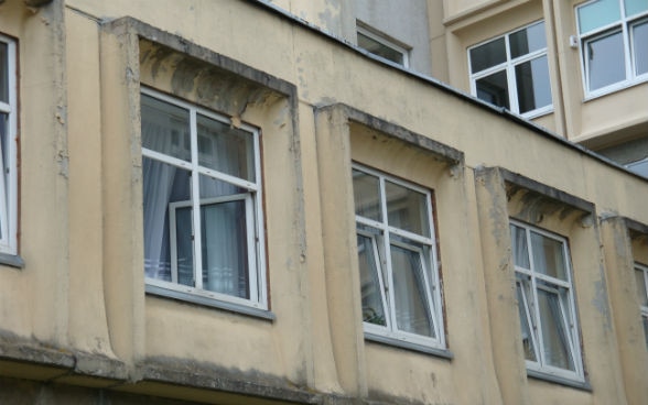 Im obersten Stock eines Gebäudes stehen drei Fenster offen. 