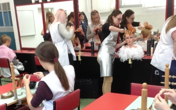 Alcune giovani donne si esercitano su dei manichini in un salone di parrucchiere.