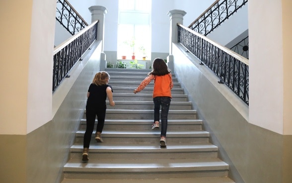 Two schoolgirls running up the stairs of a renovated school building.