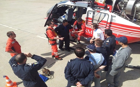 Männer stehen auf einem Flugplatz neben einem Helikopter. 