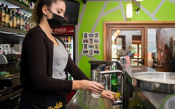 A woman behind a bar fills a glass with water from the tap.