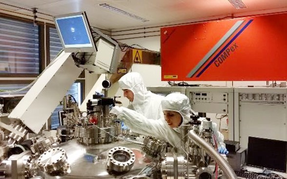 Un chercheur et une chercheuse vêtus de combinaisons de protection travaillent sur une machine.