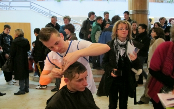 A young man demonstrates the hairdressing trade at a careers guidance event.