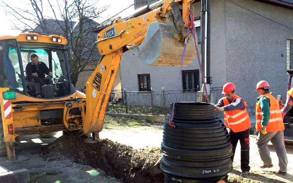 Un homme dans une pelleteuse et trois autres ouvriers travaillent sur un réseau de canalisation.